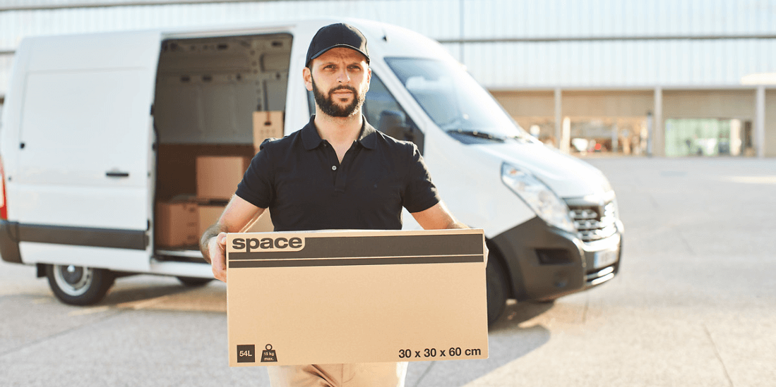 Un homme porte un carton, avec un camion derrière lui